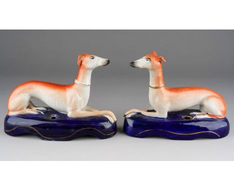 A pair of 19th Century Staffordshire quill holders modelled as recumbent greyhounds on navy oval bases, gilt heightened, repa