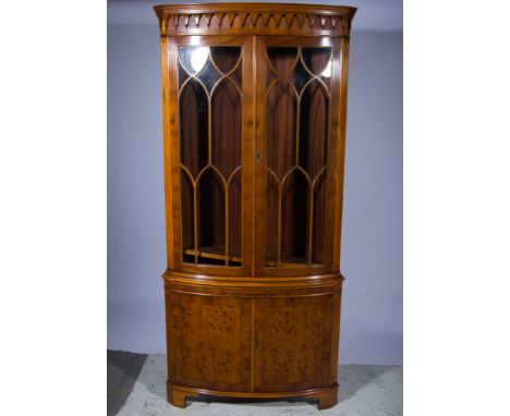 Reproduction yew wood freestanding corner cabinet, palmette frieze, lancet glazed doors enclosing two shelves, the base with 