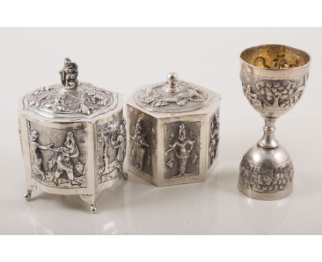 Two Eastern white metal caddy boxes, one of serpentine form repousse decorated with fields of dancing figures, raised on supp