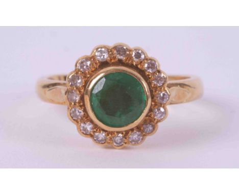 An 18ct yellow gold cluster ring set with a round cut emerald, approx. 0.75 carats in a rub over setting surrounded by small 