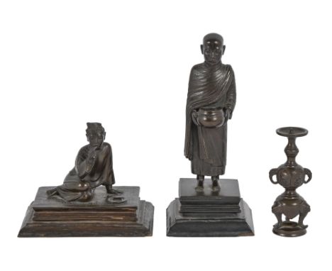 A Burmese bronze figure of a Buddhist monk, collecting arms, on an ebonised base with trade label for Combes Co Ltd Rangoon, 