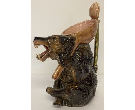 A large vintage ceramic majolica glaze honey bear jug with large spoon shaped handle. Dark brown coloured bear holding a pink