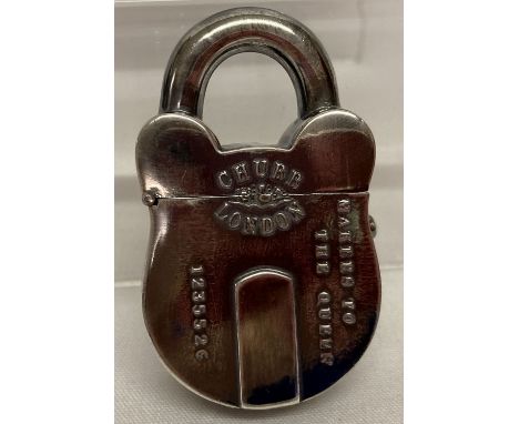 A white metal vesta case in the shape of a padlock, with push button opening. Striking panel to underside. Marked "Chubb, Lon
