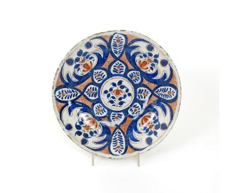 A large English delftware charger, c.1730-40, painted in blue and red with a design of stylized peony sprays in and around a 