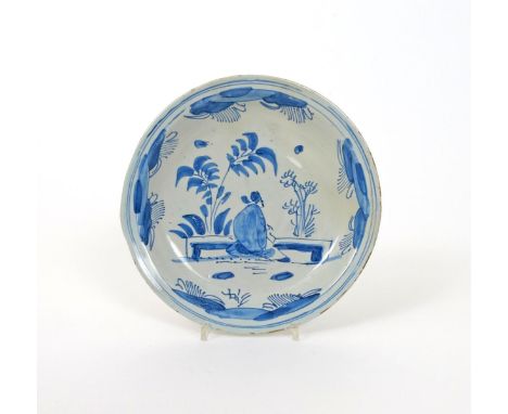 A Brislington delftware plate, c.1670-80, painted with a Chinese figure seated by a low table with bamboo beyond, a section o