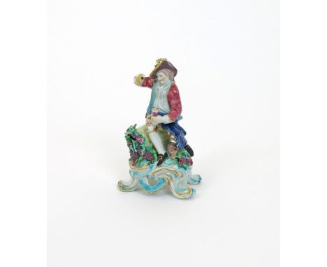 A Bow figure of Autumn, c.1760-65, modelled as a vintner seated on an upturned basket of grapes, holding a goblet in his left