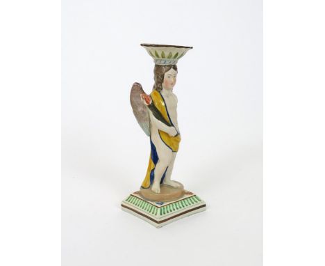 A pearlware figural candlestick, early 19th century, formed as a winged putto carrying a flaming torch, the sconce issuing fr