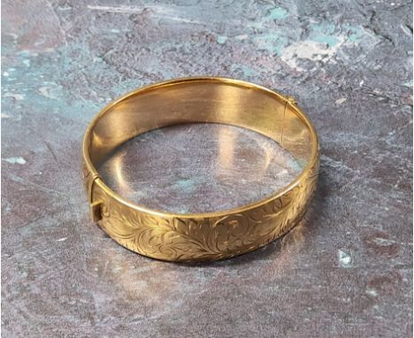 A 9ct gold hinged bangle, chased &amp; engraved with foliate scrolls, (it does not have a metal core) the inner band stamped 