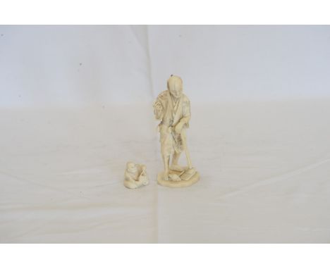 An early 20th century Japanese carved ivory figure of a gentleman holding a rustic garden tool with a bird at his feet and a 