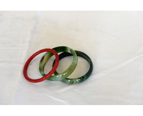 Two simulated jade bangles and an oriental cinnabar bangle with stylised flower head decoration.  Est £30-50