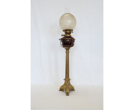 A 19th century oil lamp with frosted and clear glass shade, dark red reservoir on a triple column stem and scroll cast paw fe