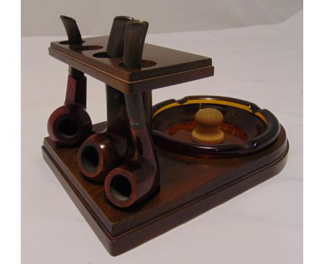 An early 20th century pipe stand shaped rectangular, the mahogany pipe stand supporting three briar pipes and a detachable gl