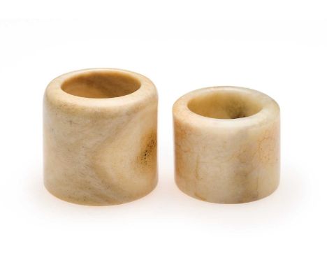 □ TWO CHINESE HARD STONE ARCHERS RINGS, QING DYNASTY, 19TH CENTURY comprising: a cream-coloured jade ring with circular inclu