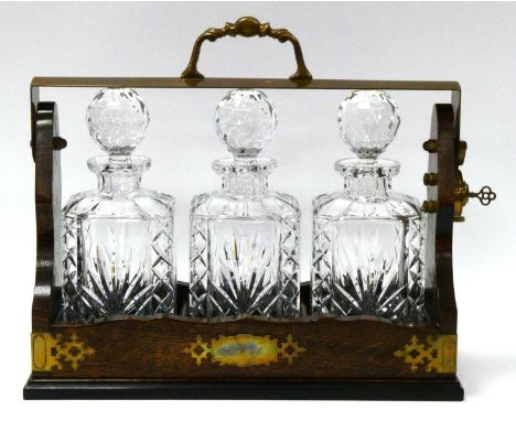 A Mid XX Century Oak Cased Tantalus, with metal mounts, containing three cut glass decanters and stoppers of rectangular form