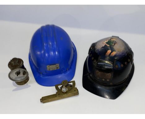 A child's black painted miner's helmet with painted illustration to the top, a blue plastic hard helmet, a Stanley of London 