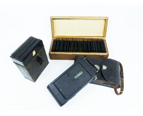 A retro Kodak camera and case together with two boxes of glass negatives featuring early 20th century domestic scenes. 
