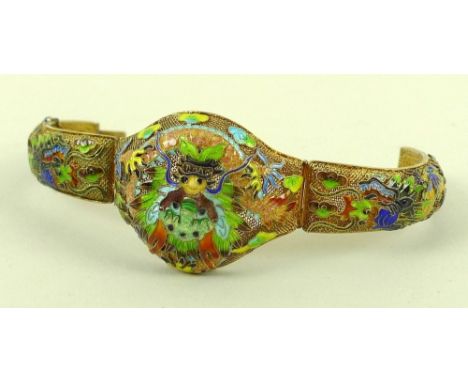 An unusual oriental gilt white metal bracelet of bangle form with two hinged sides, to the central the head of a Chinese drag
