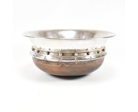 An Arts and Crafts hallmarked silver and hardwood bowl. The silver bowl having a planished finish and sitting on a hardwood b