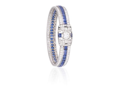 AN ART DECO DIAMOND AND SAPPHIRE BANGLE BRACELET, CIRCA 1920Millegrain-set with a central old cushion-shaped diamond within a