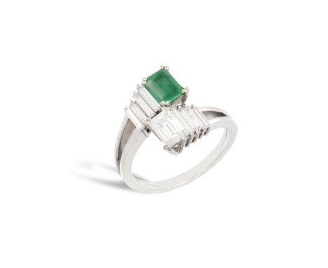 AN EMERALD AND DIAMOND RING, CIRCA 1970Of crossover design, centring upon a rectangular-shaped diamond and emerald, within a 