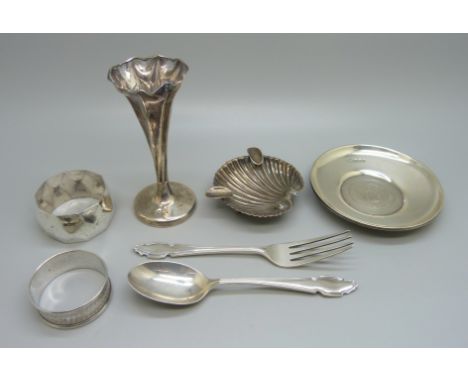 Six silver items; a vase, two napkin rings, dish, a fork and a spoon, and a white metal shell shaped dish, total weight 196g 