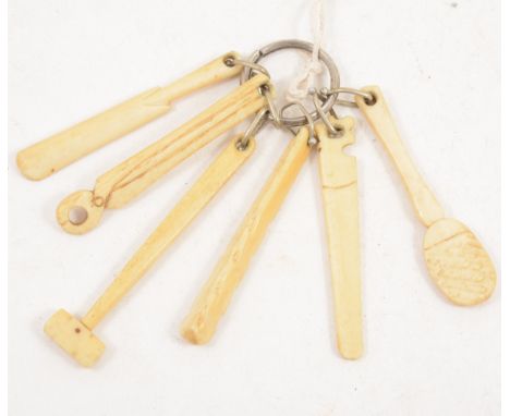 A carved bone teething ring, in the shape of carpenter’s tools, a club and a cricket bat, 9cm.