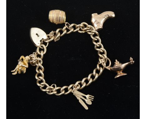 A 9 carat yellow gold solid curb link charm bracelet fitted with a padlock fastener, five charms attached and one loose, a ba
