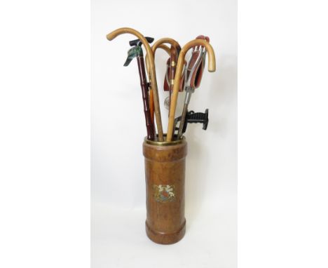 A brown leather artillery shell case stick stand with printed coat of arms and containing a selection of modern walking stick