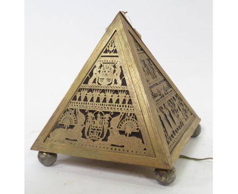 A brass pyramid shaped table lamp, each side having red glass behind cut out Egyptian panels, on four ball supports, approxim