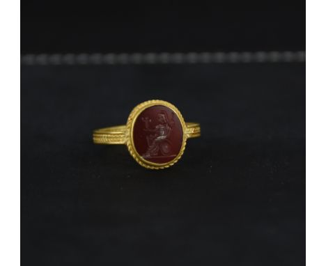 A cornelian intaglio, of a seated Roman figure admiring a statuette, in a gold ring mount with corded decoration to the head 