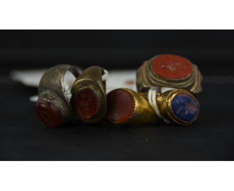 A collection of four intaglio mounted metal rings, one gilded; and an agate set metal ring