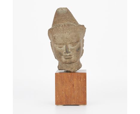 A Khmer greystone head of Buddha, likely 13th to 14th century. The face is carved with a subtle smile and the figure wears an