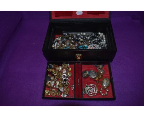 A vintage black jewellery case containing a selection of costume jewellery including brooches, clip earrings and strings of b