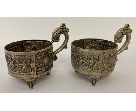 A Pair of Chinese white metal cup holders with dragon shaped handles and raised on tripod feet. Approx. 6.5cm diameter. 