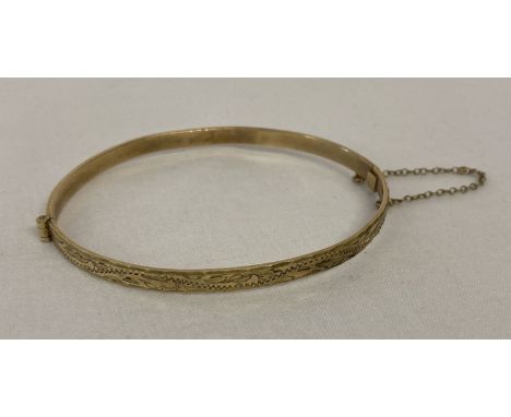 A 9ct rolled gold hinged bangle with engraved detail to one half. Complete with safety chain.  