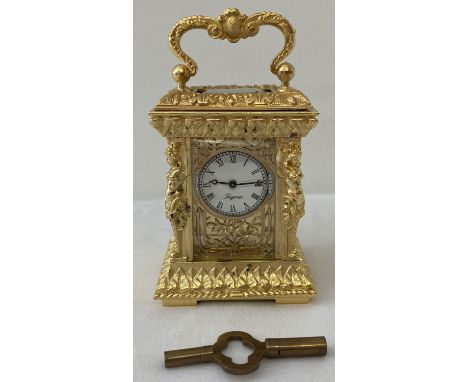 A heavily gilded ornamental miniature carriage clock with enamelled face. Classical figural column design detail to corners. 