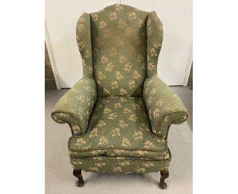 A vintage wing back chair with green &amp; gold upholstery and wooden cabriole feet.  