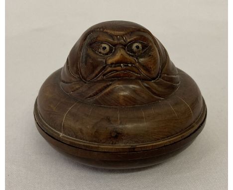 A small circular wooden Japanese trinket pot with carved figural detail to top. Signed mother of pearl disc set into base. Ap