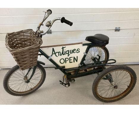A vintage 3 wheeled tricycle with central advertising panel. Painted green, with front basket. 