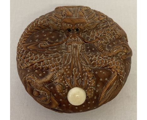 A circular shaped carved wooden pot with dragon detail. Small signed mother of pearl insert to base. Approx. 7cm diameter.