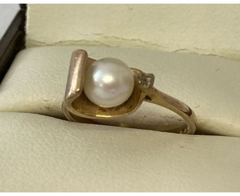 A contemporary design 9ct gold ring set with a single pearl. With a side mount for a single small round stone, Stone missing.