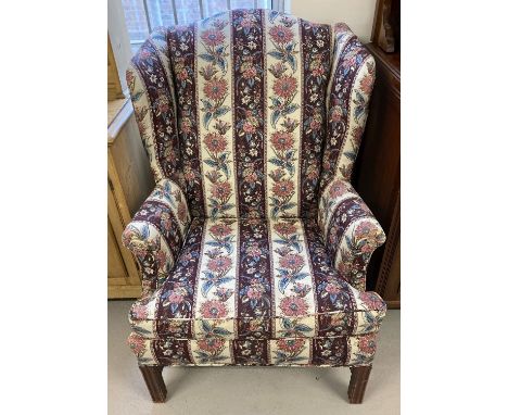 A vintage wooden framed wing back armchair with floral and maroon striped upholstery.  