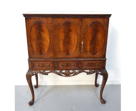 MAHOGANY DRINKS CABINETthe moulded top above a carved frieze with three oval panelled doors opening to reveal an illuminated 