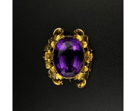 An amethyst brooch with a central cut cabochon stone set into a floral Rococo style yellow metal surround. (Tests as 14ct gol