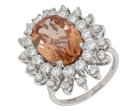 A topaz and diamond cluster ring, 1975, the oval-cut sherry-coloured topaz within a double cluster surround of brilliant-cut 