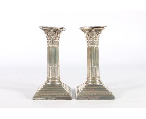 Pair of silver dwarf candlesticks of Corinthian column form raised on stepped bases by William Hutton &amp; Sons Ltd, London 