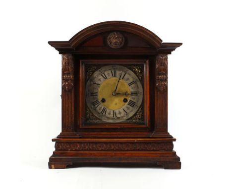A late 19th century mantel clock, the silvered chapter ring with black Roman numerals within a carved case of architectural f