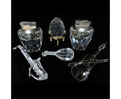 A Swarovski crystal table lighter, 8.5cm tall, together with an egg paperweight on a stand, a model of a violin, a saxophone 