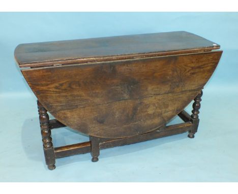 An antique oak drop-leaf dining table, the oval top above an end frieze drawer, on bobbin-turned legs and gates joined by str