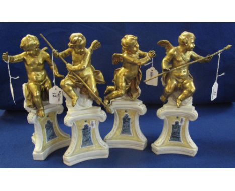 Set of four ceramic and metal cherubs upon scrolled plinths, in various poses, the cherubs over-gilded. Unmarked, approx 31cm